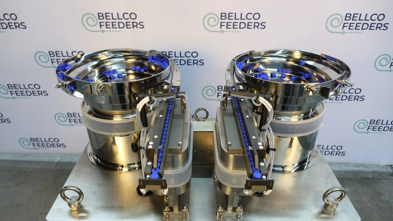 Twin stainless vibratory bowl feeders orienting blue closures, on a Bellco Feeders backdrop