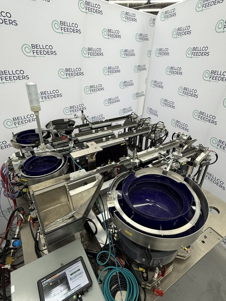 Five Bellco feeders on a single shared baseplate: four vibratory bowls plus a step feeder, running together under eighty decibels