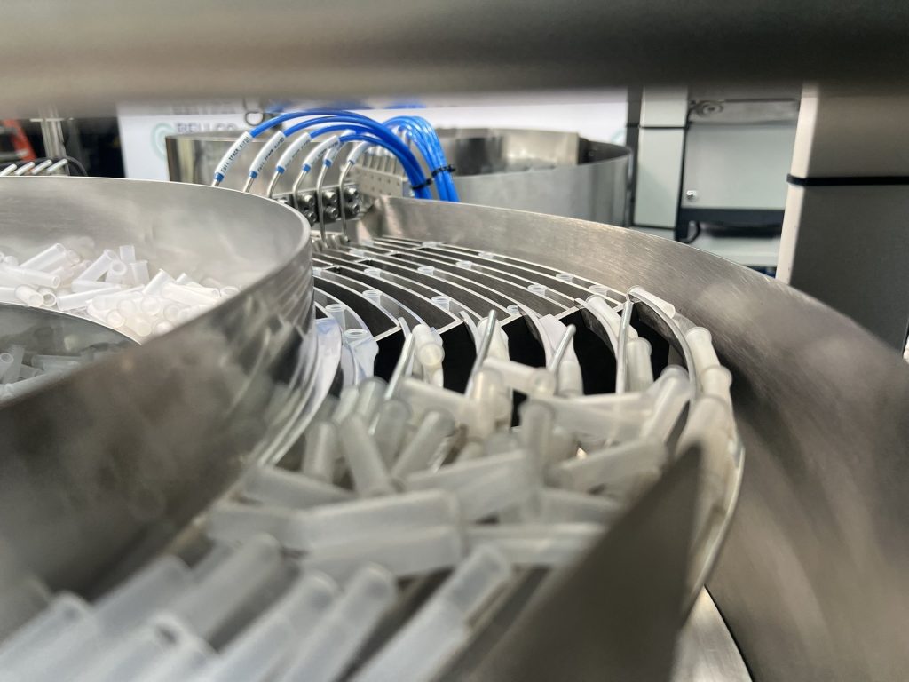 White molded medical components traveling up the tooled track of a Bellco stainless bowl