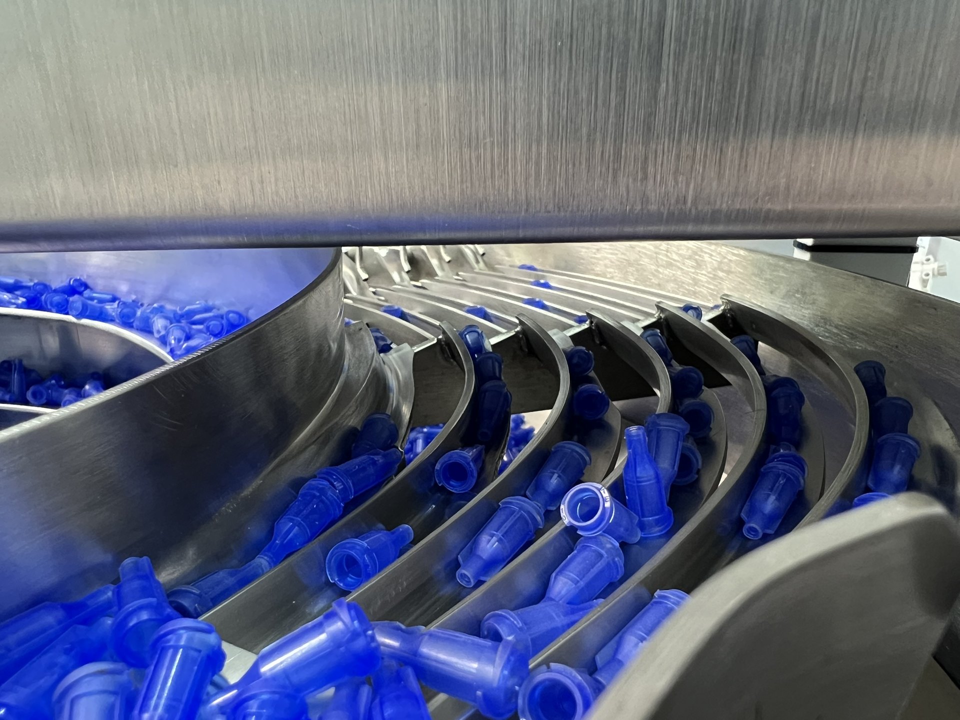 Blue molded plastic components lined up on the outfeed track of a Bellco vibratory bowl feeder