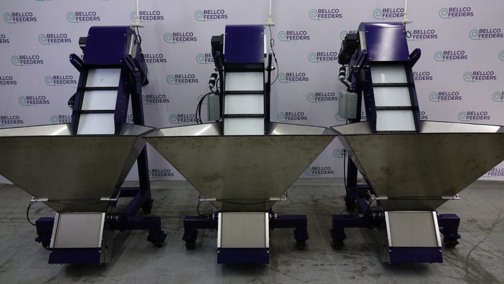 Three Bellco elevating conveyor hoppers lined up on the shop floor before shipment