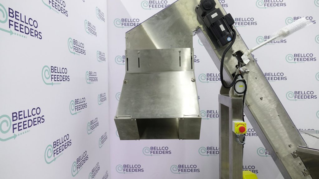 Discharge chute on a Bellco elevated conveyor hopper, angled to drop parts into a feeder bowl