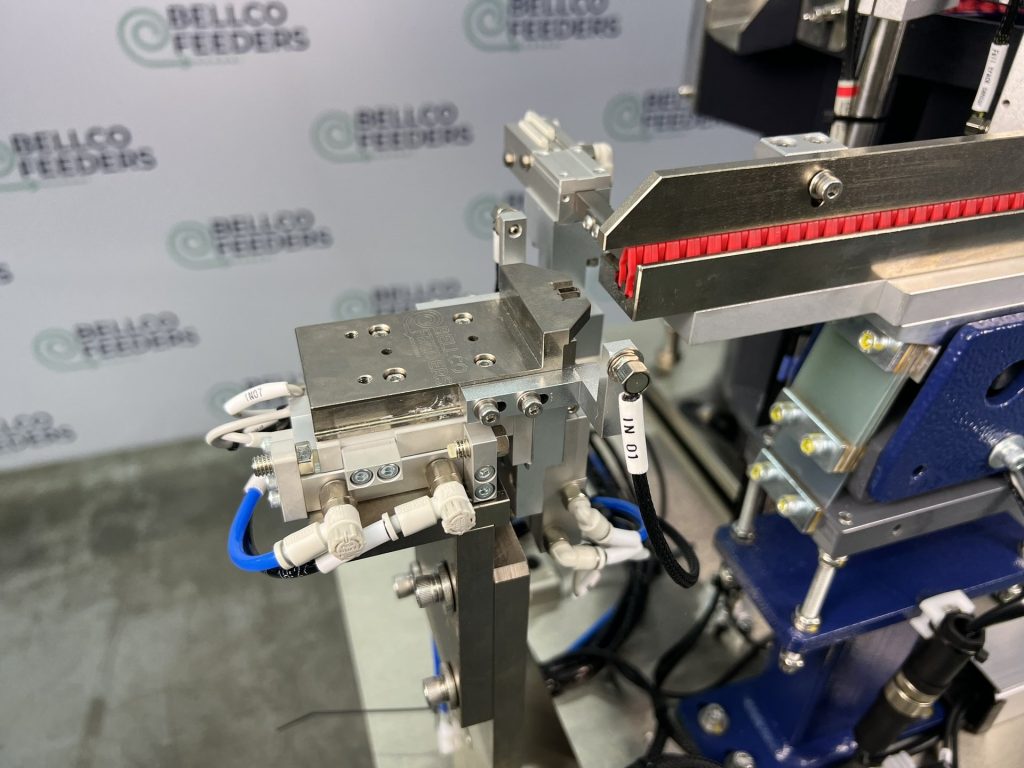 Pull-back escapement and lit inspection bar at the outfeed of a Bellco vibratory feeder