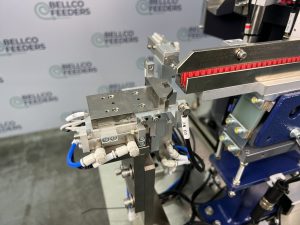 Pull-back escapement and lit inspection bar at the outfeed of a Bellco vibratory feeder