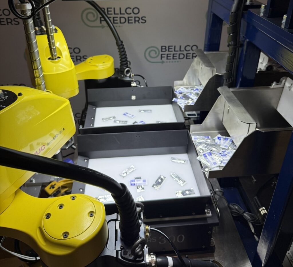 FANUC robot picking parts from the backlit platform of a Bellco Flex feeder inside a guarded cell