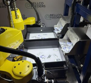 FANUC robot picking parts from the backlit platform of a Bellco Flex feeder inside a guarded cell