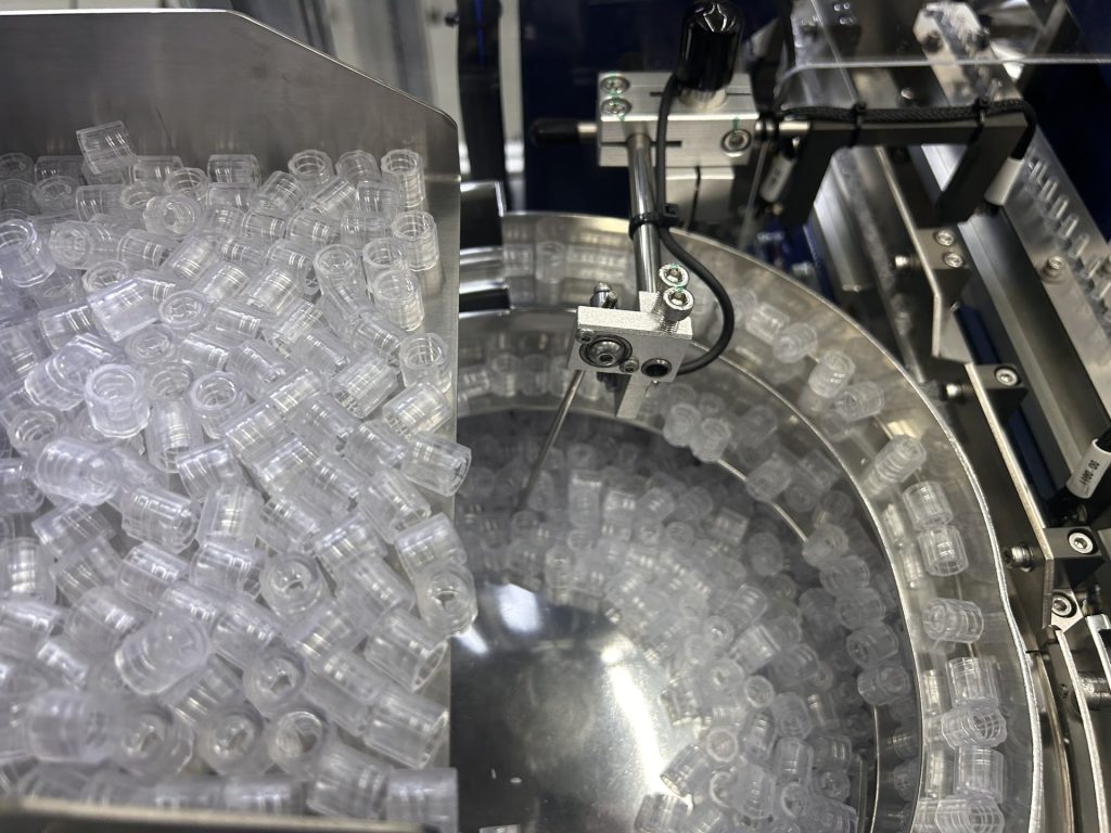 Clear plastic components circulating in a Bellco bowl feeder fed from a bulk hopper above