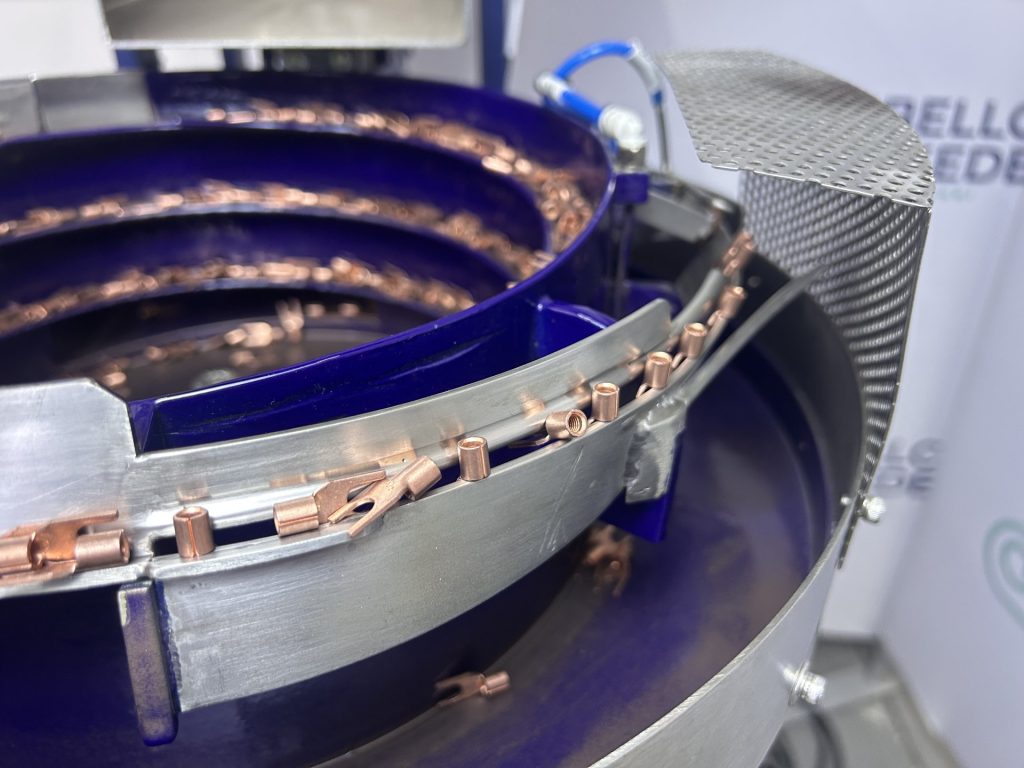 Close view of copper ring terminals lined up on the outfeed track of a Bellco vibratory bowl