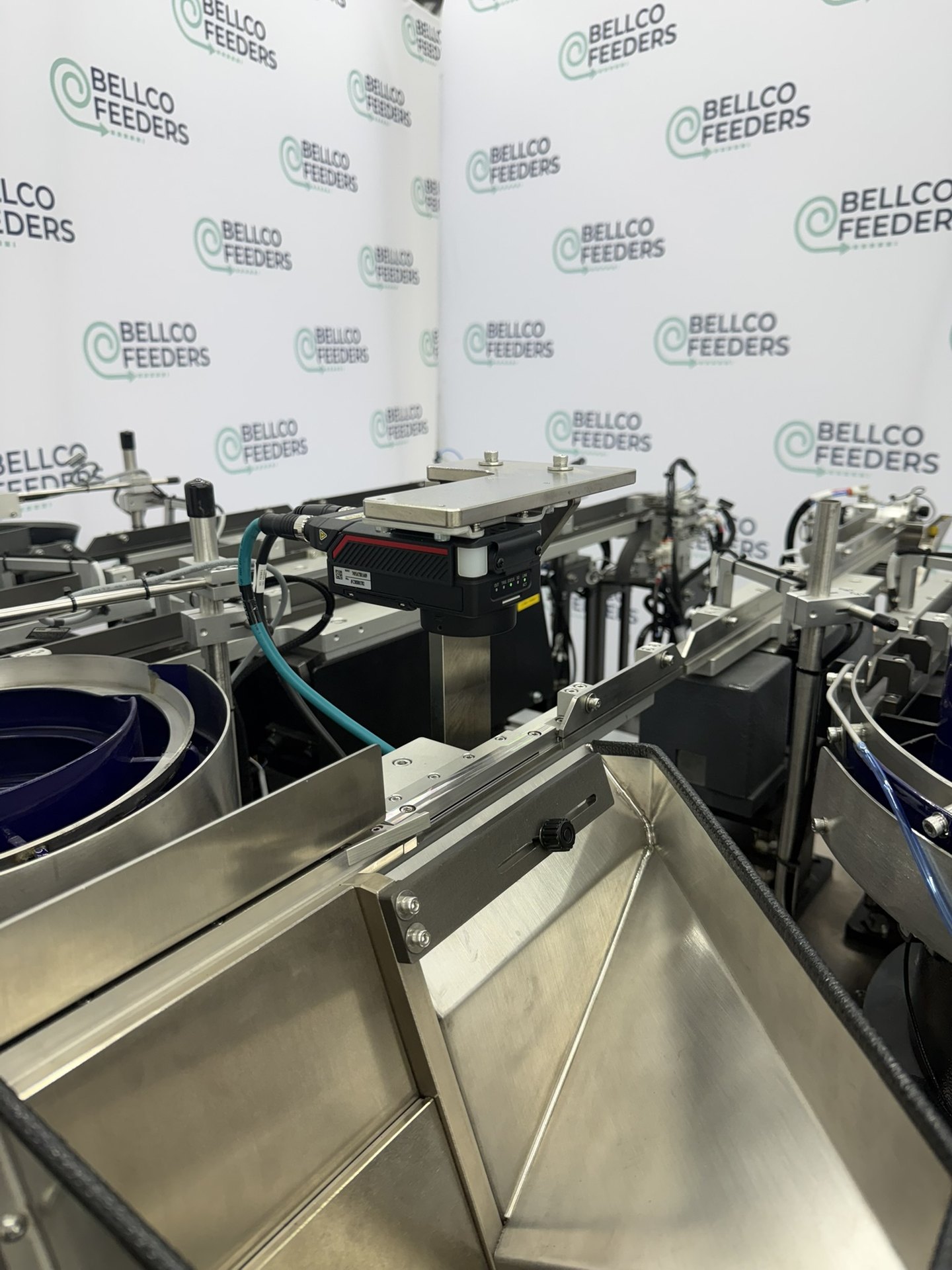 Tabletop Bellco step feeder with a stainless loading hopper, built to sit inside an existing robotic assembly cell